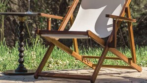 A wooden lounge chair with a white cushion, positioned on a paved area with grass and trees in the background. - Casa Pino-private family villa with pool in Corfu, close to beaches/water park (Corfu)