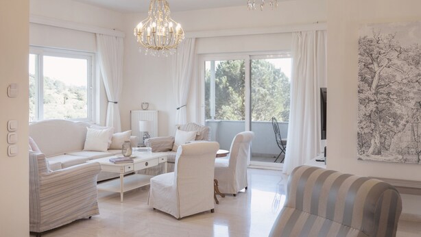 A spacious living room with a white sofa, armchairs, a coffee table, and a striped couch. There are two chandeliers, large windows with curtains, and a wall-mounted flat-screen TV. - Casa Pino-private family villa with pool in Corfu, close to beaches/water park (Corfu)
