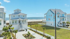 A coastal property with multiple buildings, a clear view of the beach, and a well-maintained lawn with palm trees. - Beautiful Second Row Beachside Home - Steps from Sand & Surf (Galveston)