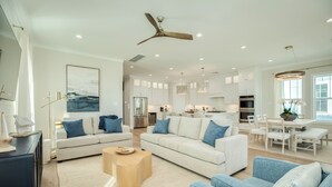 A spacious living area with a large white sofa, blue accent pillows, a wooden coffee table, and a ceiling fan. - Beautiful Second Row Beachside Home - Steps from Sand & Surf (Galveston)