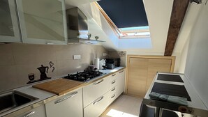 Una cocina moderna con tragaluz, armarios blancos, estufa a gas y espacio para preparar café.