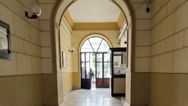 Un pasillo con techo alto y un arco que conduce a una habitación luminosa.