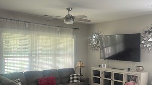 Ett vardagsrum med en soffa, en pall och en platt-TV som är monterad på väggen.