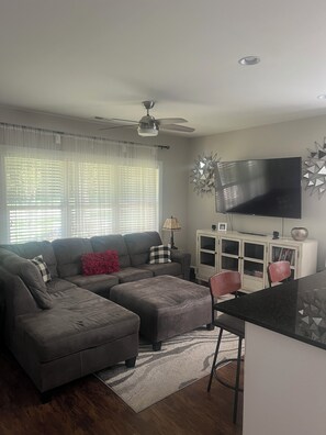 A living room with a sofa, ottoman, and a flat-screen TV mounted on the wall. - Private 1-Bedroom Retreat (Charlotte)