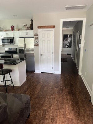 A modern kitchen with stainless steel appliances, a dining area with a bar stool, and a hallway leading to a bedroom. - Private 1-Bedroom Retreat (Charlotte)