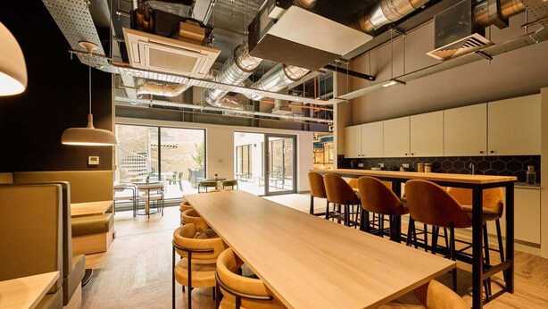 Un intérieur moderne avec une longue table en bois, des chaises rembourrées et un coin cuisine.