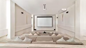 Ein modernes, minimalistisches Zimmer mit einem großen Flachbildfernseher an der Wand, einer Couch mit Kissen und einer Decken-Klimaanlage.