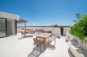 A rooftop terrace with outdoor seating, a glass door entrance, and a view of the city skyline. - Tulum Oasis 2-Level Penthouse (Q.R.)