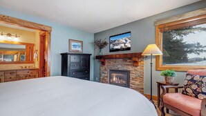 Une chambre avec une cheminée, un lit, une commode et une fenêtre donnant sur des arbres.