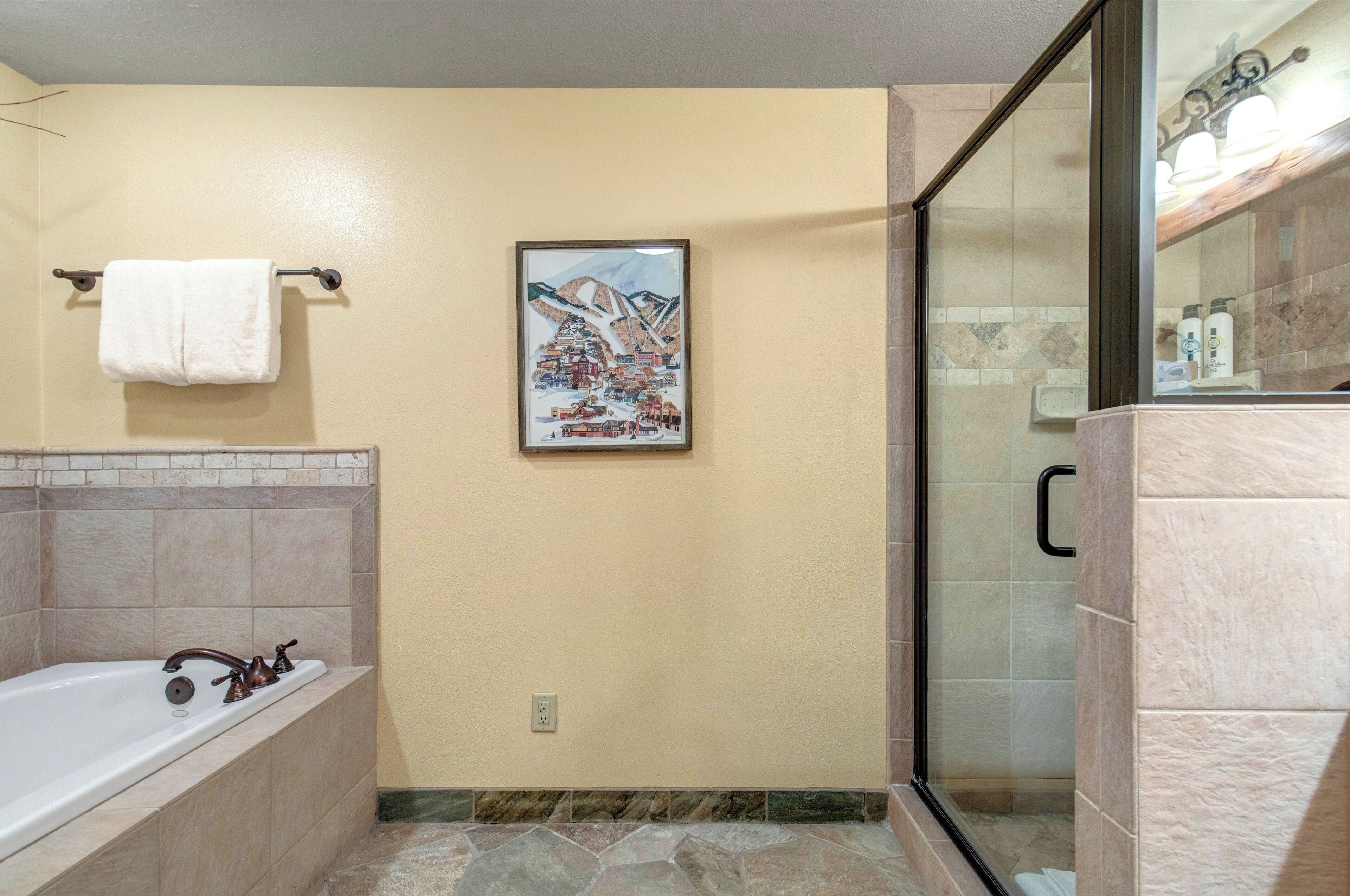A bathroom with a bathtub, a glass shower enclosure, and a framed picture on the wall.