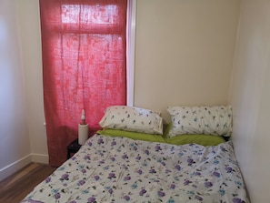 Une chambre à coucher avec une couvre-lit à motifs floraux, des coussins verts et un rideau rouge.