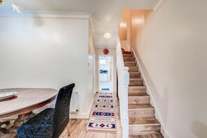 A hallway with a dining table, chairs, a patterned rug, and a wooden staircase. - 3 Bed House - Sleeps 6 - Garden - Central London (London)