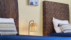 Ein Bett mit blauer Bettdecke, zwei Kissen, einem gewobenen Kopfteil und einer Stehlampe.