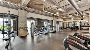 A gym with treadmills, weight machines, and a concrete ceiling. - Dallas Skyline View Flat w/ Pool, Gym & Free Parking (Dallas)
