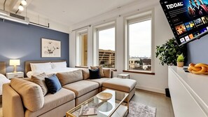 A modern hotel room with a large bed, a sofa, a glass coffee table, and a TV mounted on the wall. - Dallas Skyline View Flat w/ Pool, Gym & Free Parking (Dallas)