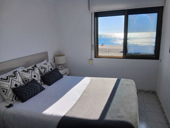 A bedroom with a bed, pillows, a nightstand, a lamp, and a window with a view of the beach. - Beachfront home with spectacular ocean views (La Cala del Moral)