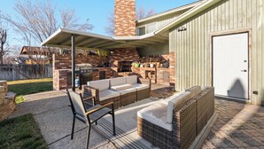 Un patio trasero con chimenea de ladrillo, mobiliario exterior y un porche cubierto.
