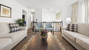 Una sala de estar con dos sofás, una mesa de centro con una planta y una escalera al fondo.