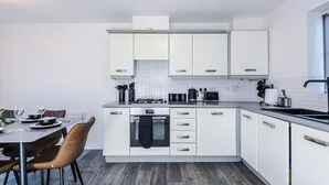 Una cucina moderna con mobili bianchi, un'isola centrale e un'area pranzo con sedie marroni.