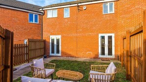 Una casa in mattoni con un cortile recintato, un patio con mobili in vimini e un'entrata doppia.