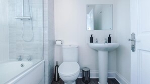 Un bagno moderno con box doccia in vetro, un water bianco, un lavabo su piedistallo e uno specchio sopra il lavabo.