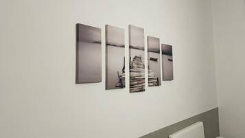 Eine Wand mit fünf rechteckigen Kunstwerken, die eine Küstenlandschaft mit einem Steg und Booten zeigen.