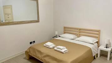 Habitación de hotel con cama, dos mesitas de noche, un espejo y una puerta.