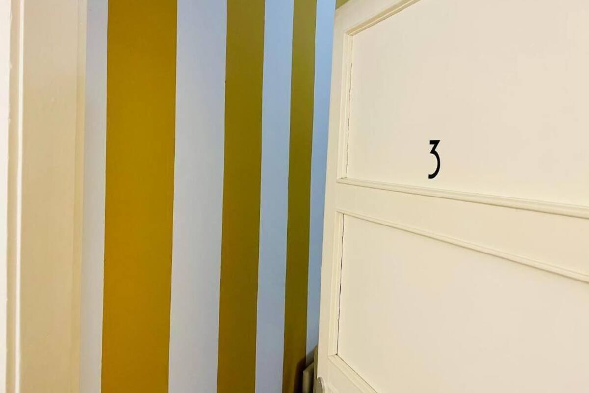 A door with the number 3, adjacent to a wall with vertical stripes in yellow, white, and light blue.
