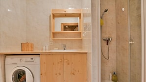 A compact bathroom with a washing machine, wooden cabinets, a sink, and a shower. - Cosy 6-person apartment in Chinaillon (Le Grand-Bornand)