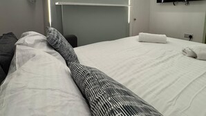 Una camera d'albergo moderna con un letto rifatto, una TV a schermo piatto a parete e una stampa botanica incorniciata.