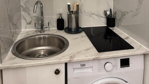 Una cucina compatta con lavello, lavatrice integrata e piano cottura a induzione nero.