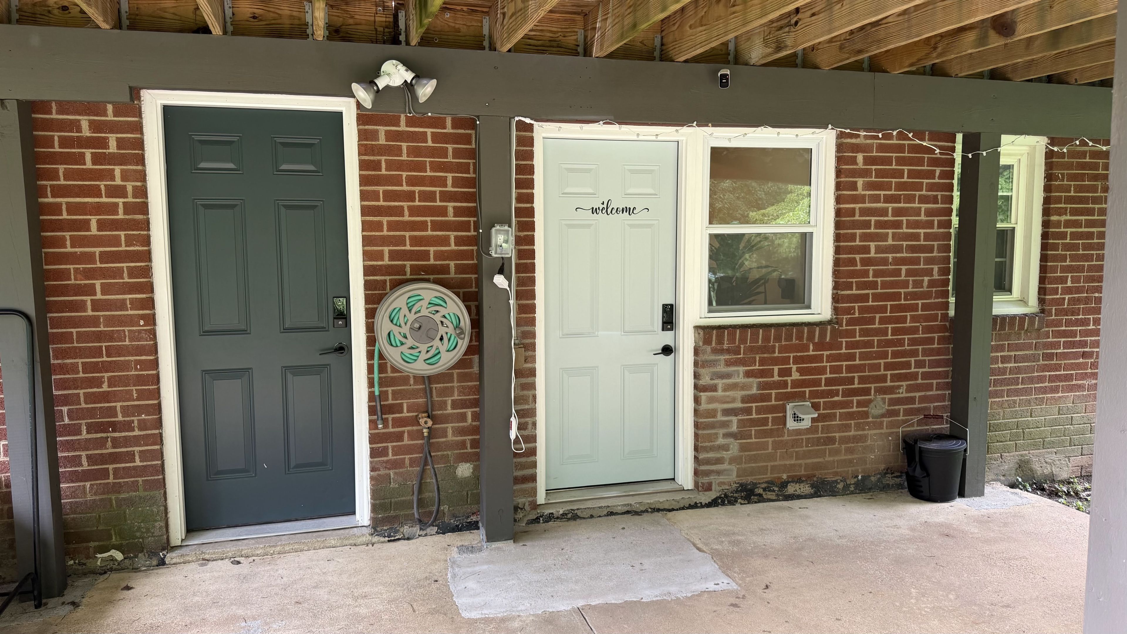 A building with two doors, one with a 'welcome' sign, a window, and a hose reel on the wall.