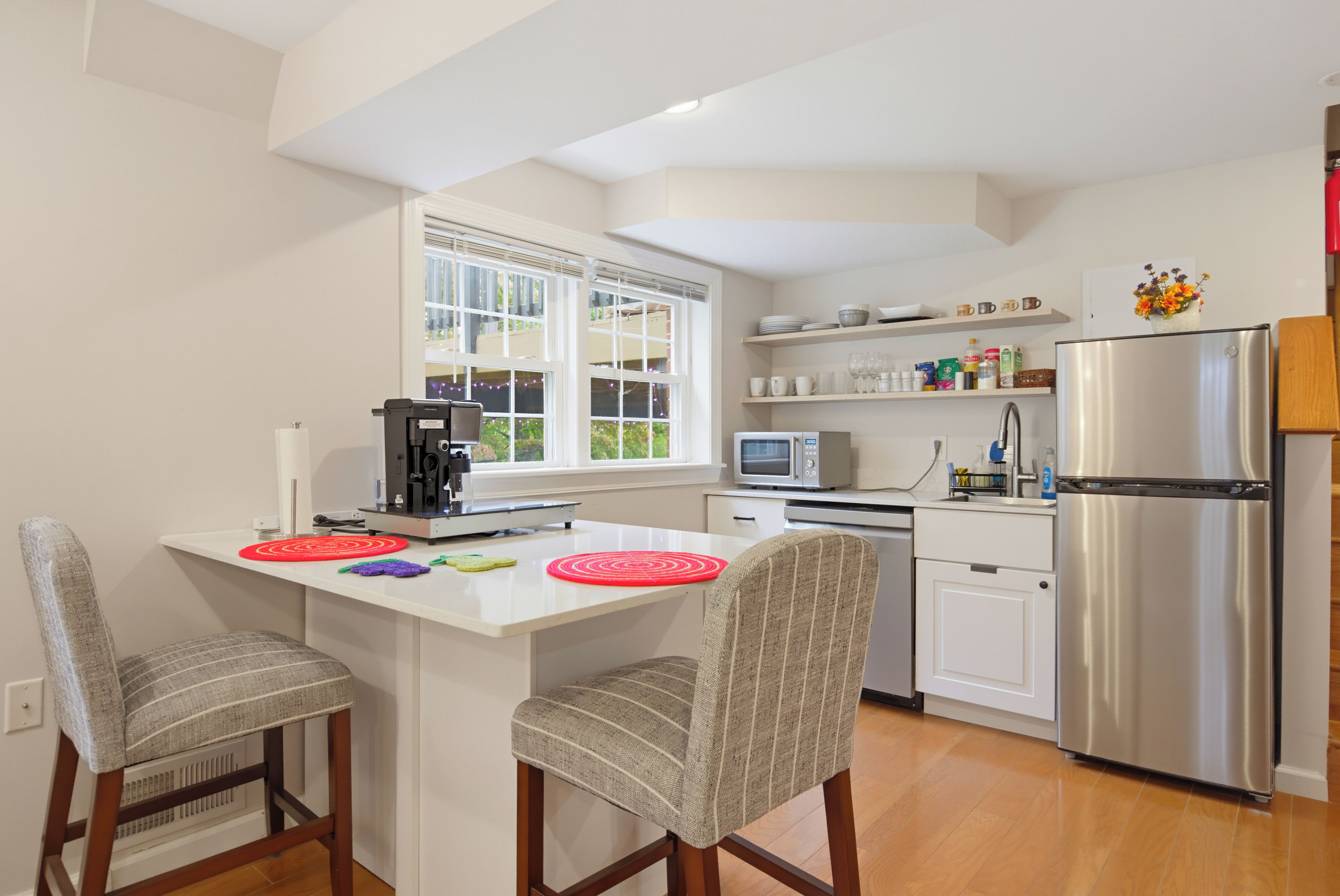 A kitchen with a central island, two chairs, a refrigerator, a microwave, and a window with blinds.