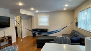A living room with a hammock, a flat-screen TV, a sofa, and a dining table.
