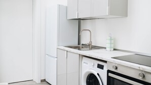 Cuina moderna amb armaris blancs, un vàter d'acer inoxidable, una rentadora i un forn encastrat.