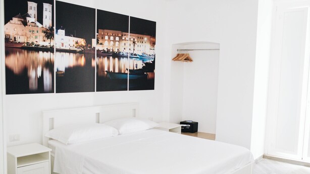 Habitació d'hotel amb un llit gran, nits blanques, un aparell de ràdio fixat a la paret i vista a un paisatge urbà de nit.