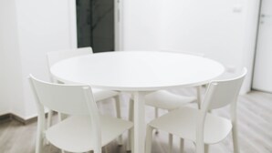Taula rodona blanca amb quatre cadires blanques en una habitació de parets blanques i terra de fusta.