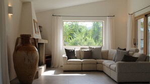 Una sala de estar con un sofá seccional color beige, un jarrón grande y una ventana con cortinas.