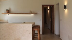 Una cocina con encimera de mármol, taburetes de madera y estante con adornos.