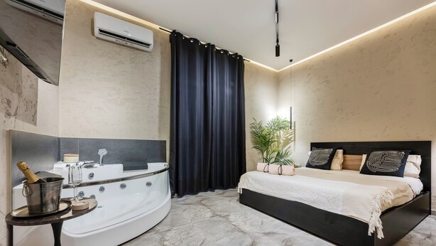 Une chambre moderne avec un grand lit, une baignoire aux formes arrondies et une petite table sur laquelle se trouve une bouteille de champagne.