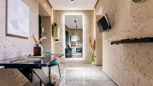 Une cuisine moderne dotée d’un îlot central, un coin repas avec une table noire et des chaises turquoise, et un couloir menant à l’espace de vie.