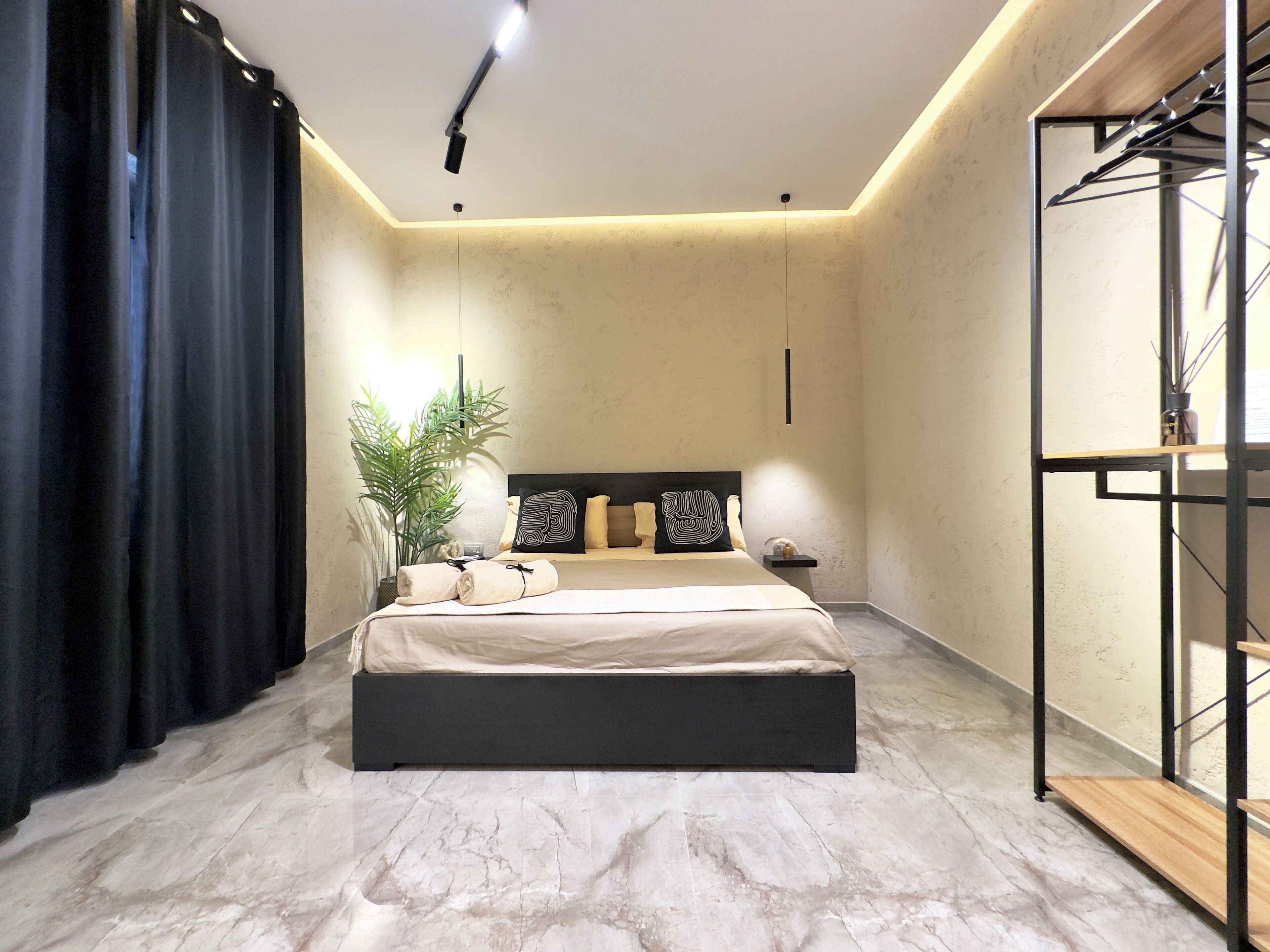A modern bedroom with a large bed, a nightstand, a potted plant, and a wardrobe.