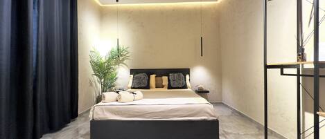 A modern bedroom with a large bed, a nightstand, a potted plant, and a wardrobe.