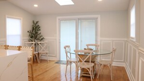 A dining area with a glass table surrounded by white chairs, a potted plant, and a white cabinet. - A Great Place To Relax -A (Uniondale)