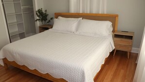 A bedroom with a wooden bed, white bedding, a nightstand, a bedside table, and a plant. - A Great Place To Relax -A (Uniondale)