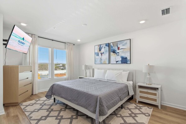 A modern bedroom with a bed, bedside tables, a TV, and abstract wall art.