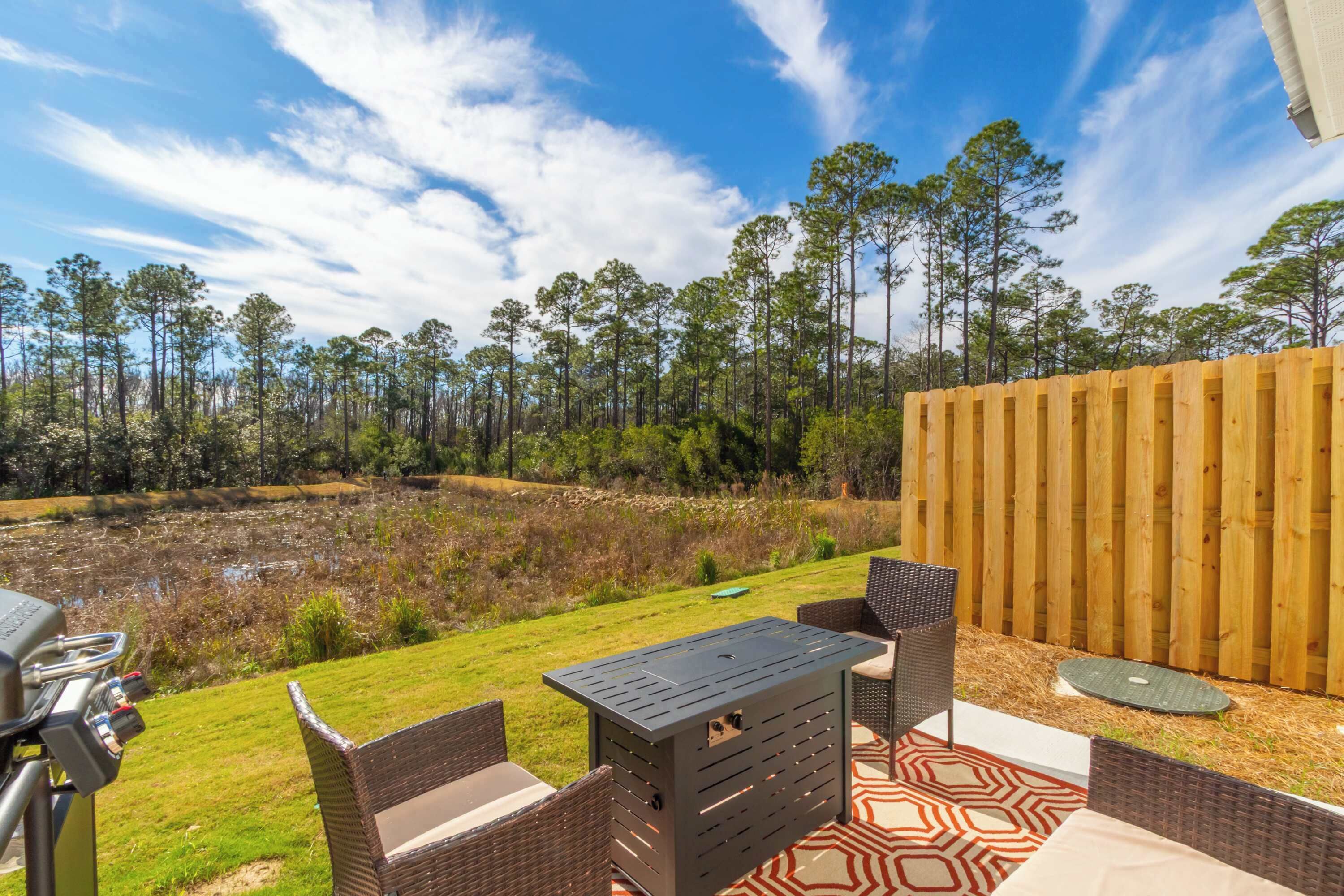 A patio area with outdoor furniture, a grill, and a view of a pond and forest.