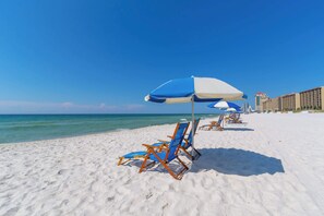 A beach with white sand and clear blue water. There are blue and white beach chairs and umbrellas.