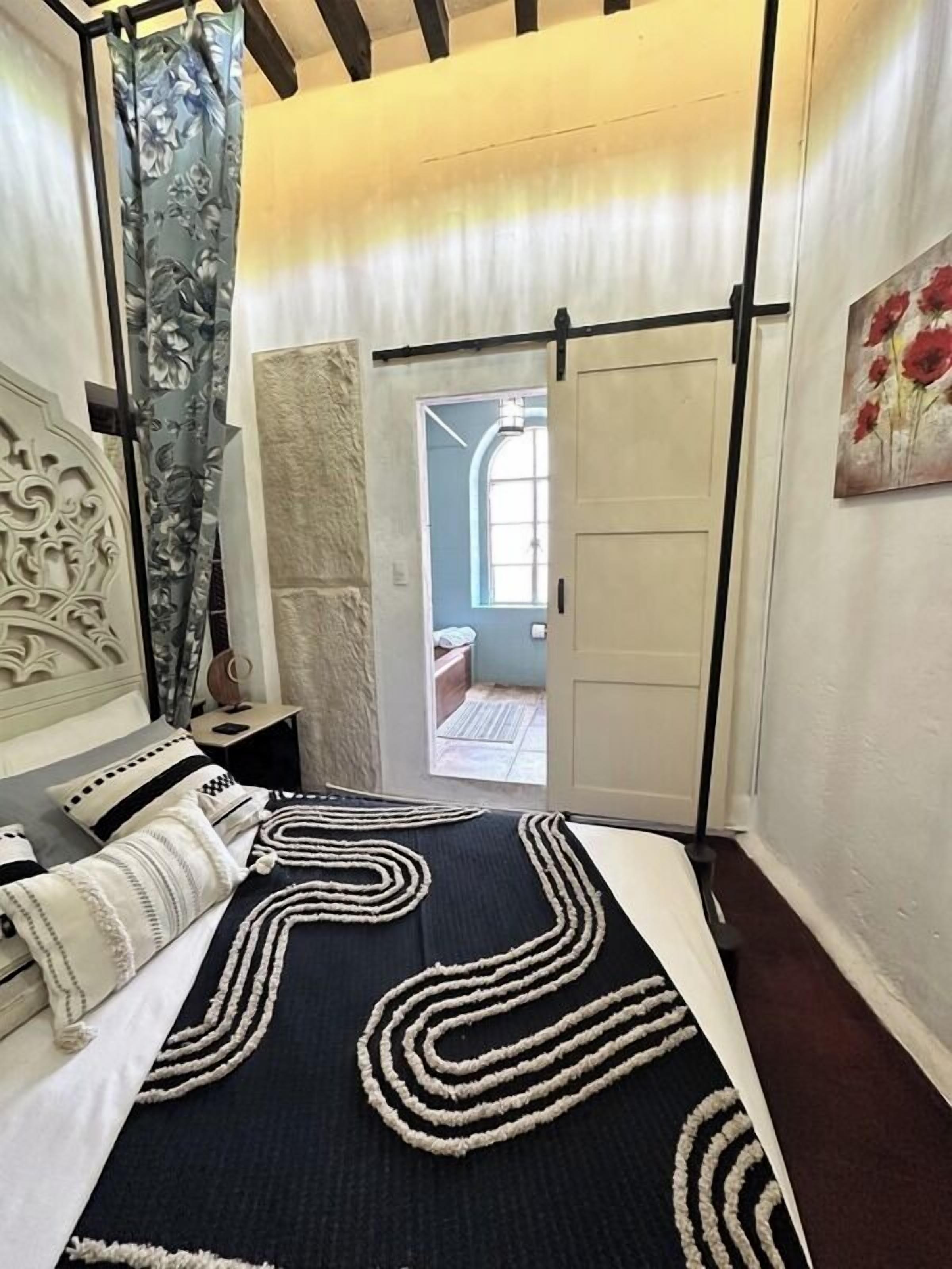 A bedroom with a bed, a nightstand, a door, and a painting.