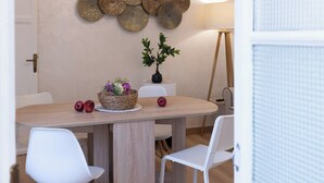 Un coin repas avec une table en bois, des chaises blanches, un élément décoratif mural et une petite plante en pot.